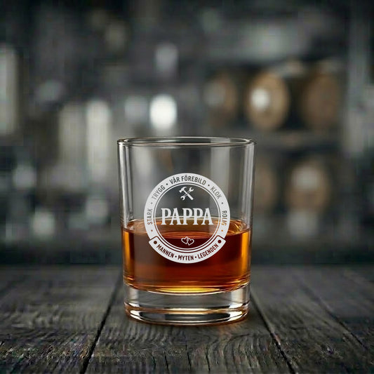 Ett graverat whiskyglas till pappa fyllt med dryck. Glaset har ett runt emblem med orden 'Mannen, Myten, Legenden' samt 'Stark, Trygg, Vår Förebild'.