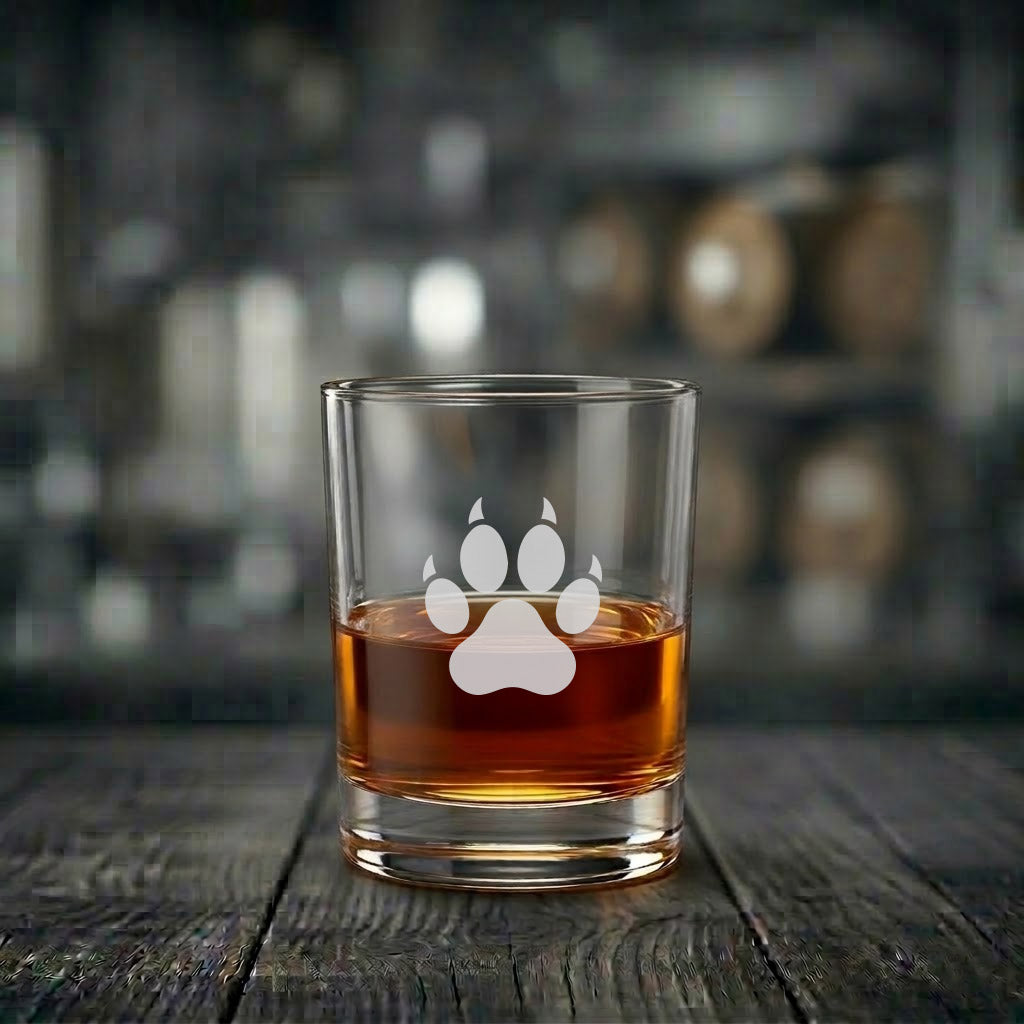 Ett exklusivt whiskyglas med en graverad djurtass, fyllt med gyllene bärnstensfärgad whisky, stående på ett mörkt och rustikt träbord.