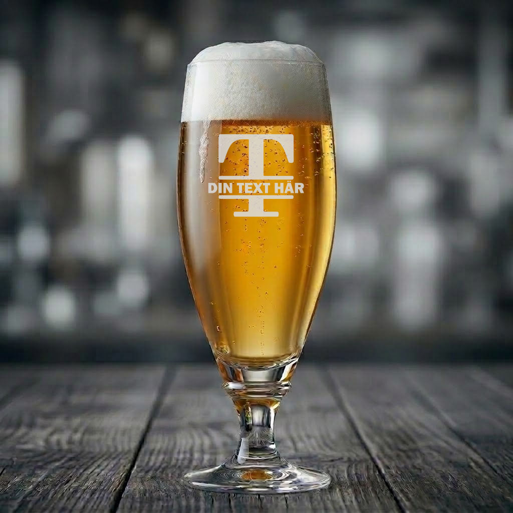 Ett ölglas på fot med öl och skumkrona, graverat med ett stort monogram för bokstaven T och en banderoll där du kan lägga till din egen personliga text.