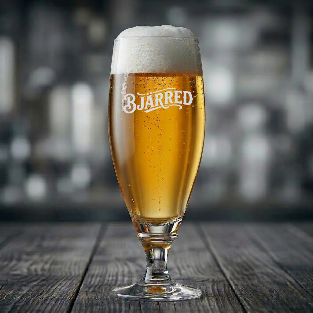 Elegant ölglas med texten Bjärred ingraverad, fyllt med gyllene öl med skumkrona på ett träbord.