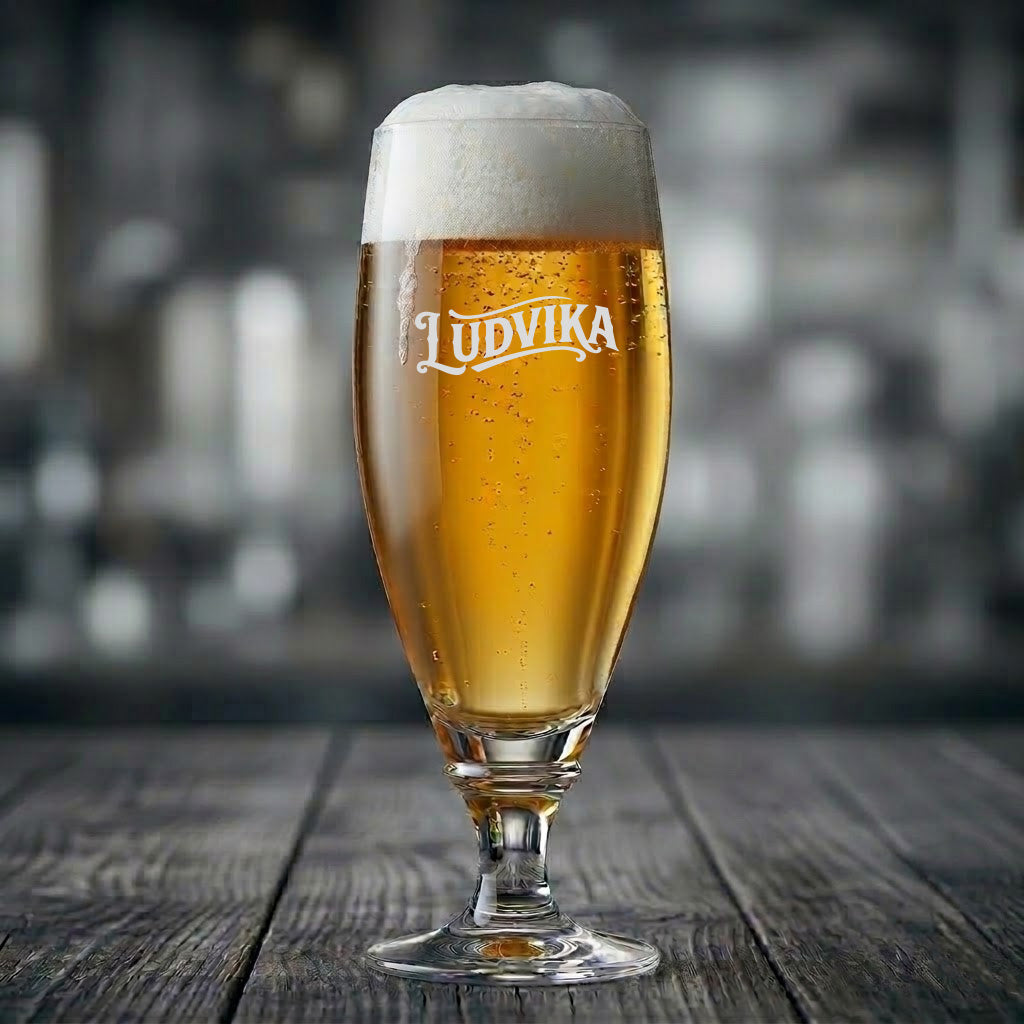 Elegant ölglas med texten Ludvika ingraverad, fyllt med gyllene öl med skumkrona på ett träbord.