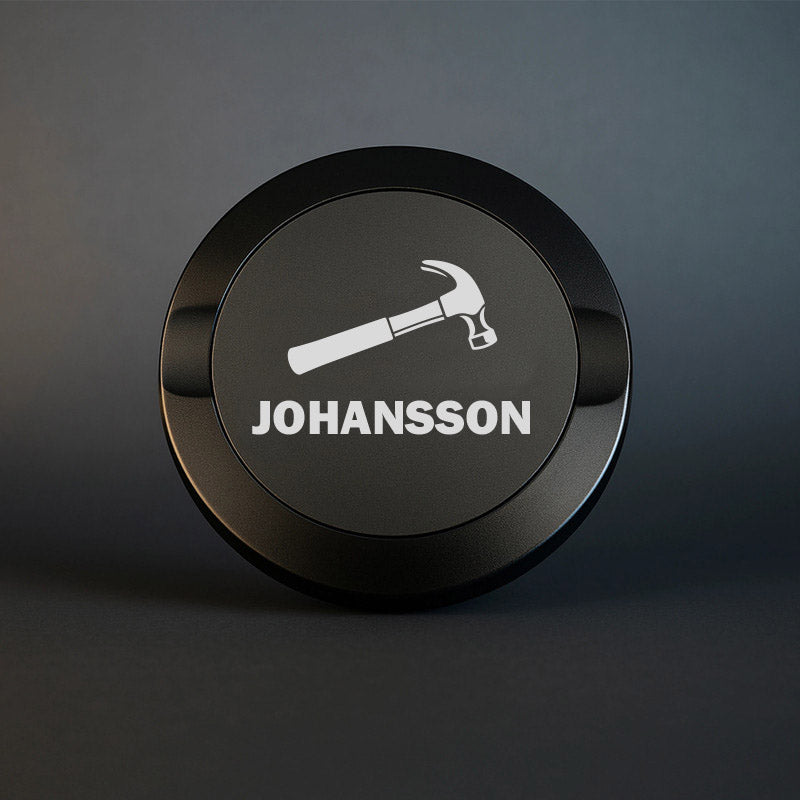 Svart graverad snusdosa i metall med motiv av en hammare och namnet Johansson.