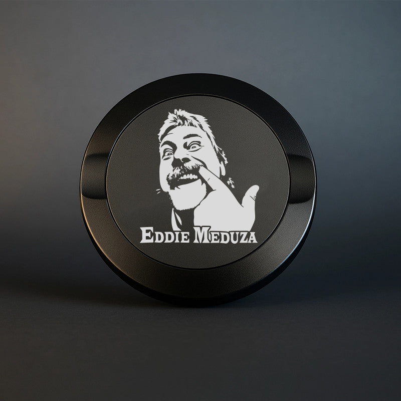 En exklusiv mattsvart snusdosa i metall med en detaljerad och knivskarp lasergravyr av artisten Eddie Meduza, placerad mot en mörk och stilren bakgrund.