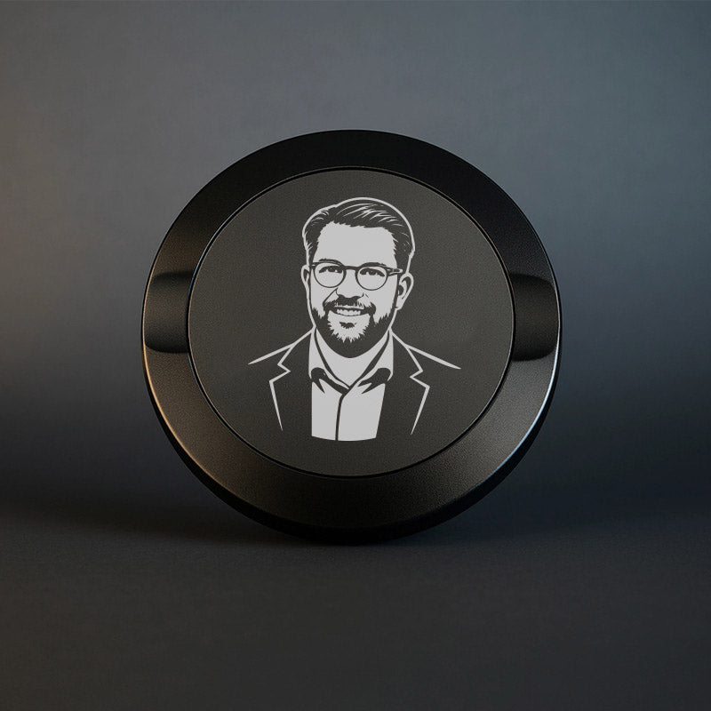 Mattsvart metall snusdosa med detaljerad gravyr av Jimmie Åkesson i kostym och glasögon. Premium snusdosa med porträtt på mörk bakgrund.