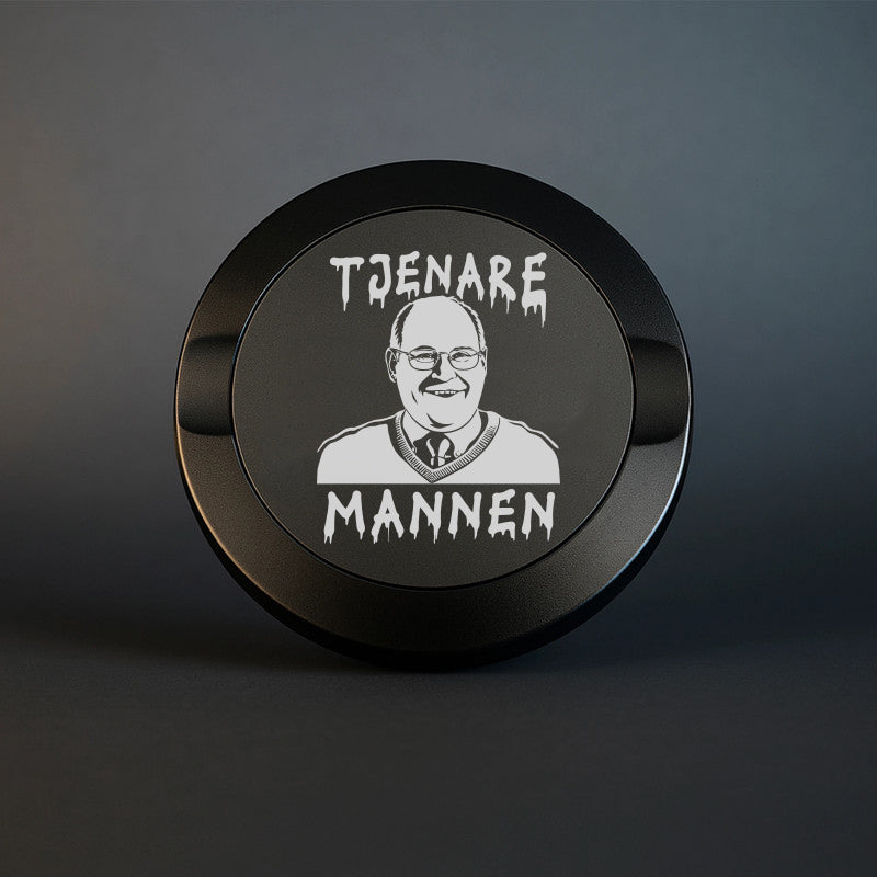 En mattsvart snusdosa i metall med knivskarp gravyr av karaktären Ove Sundberg och texten "TJENARE MANNEN" i en droppande font, fotograferad mot en mörk och stilren bakgrund.