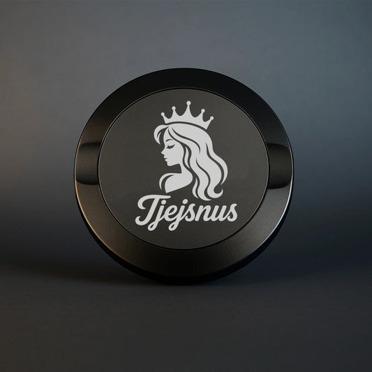 Mattsvart snusdosa i metall med en detaljerad vit gravyr av en kvinna med krona och texten Tjejsnus, fotograferad mot en stilren och mörk bakgrund.