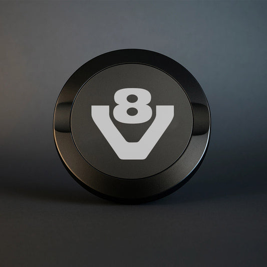 Stilren mattsvart snusdosa i metall med en knivskarp V8-gravyr på locket, placerad på ett mörkt och stilrent underlag.