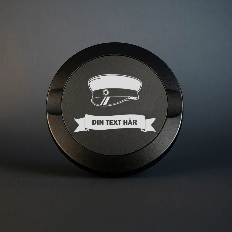 Svart snusdosa i metall med ingraverad studentmössa och en banderoll med plats för valfri text. Perfekt som studentpresent.